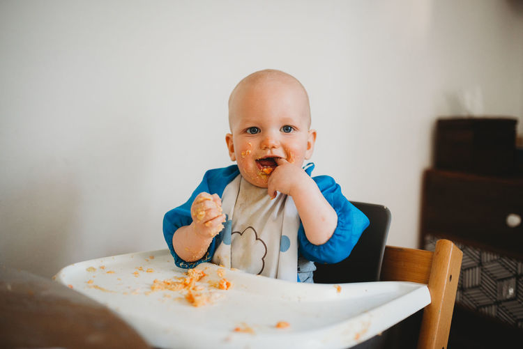 Adorable baby learning how to eat making a mess finger in mouth