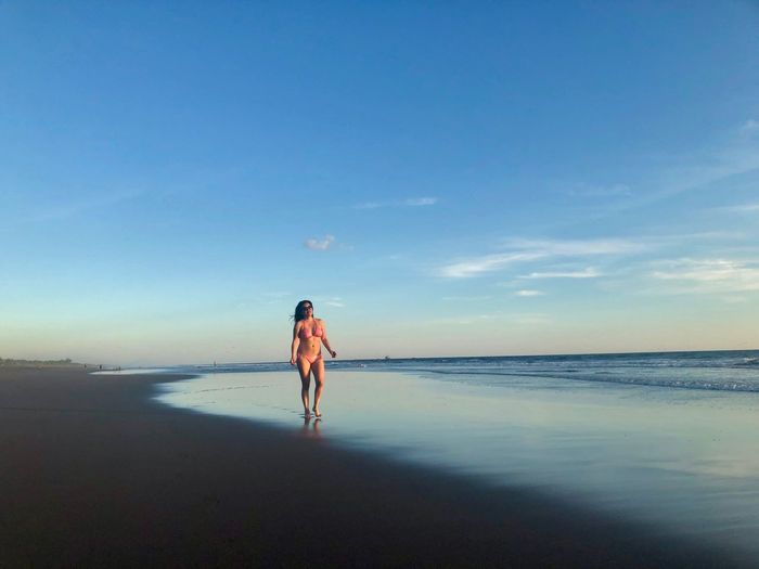Full length of woman wearing bikini standing on beach against sky