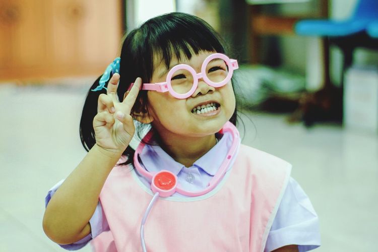 Close-up of cute girl in doctor costume gesturing peace sign at home