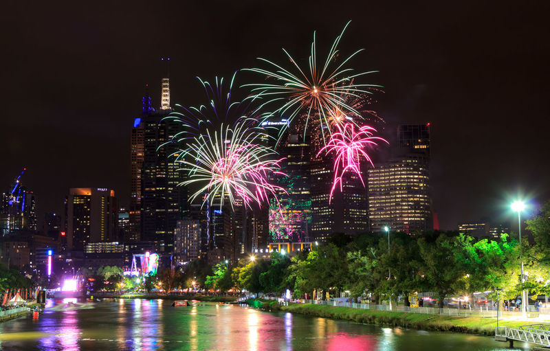 Firework display over yarra river by melbourne city buildings against sky at night
