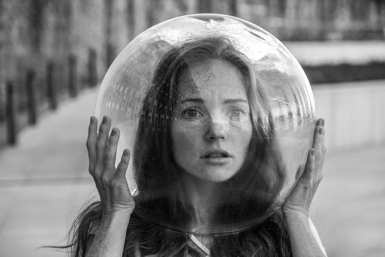 Portrait of scared young woman wearing glass helmet in head on sidewalk