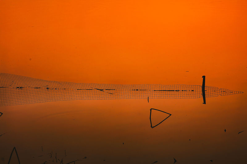 Silhouette birds on wooden post against orange sky