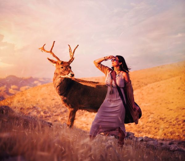 Woman standing by deer on land against sky