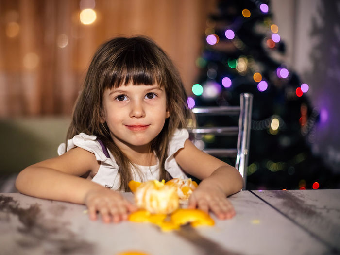 Portrait of cute girl with illuminated christmas lights on table