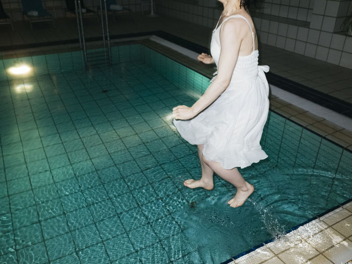 Low section of woman jumping in swimming pool at night