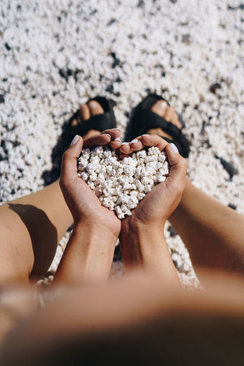 Low section of woman holding pebbles in heart shaped hands at beach
