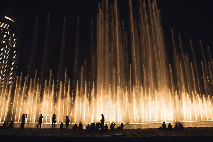Silhouette people against illuminated fountain at night