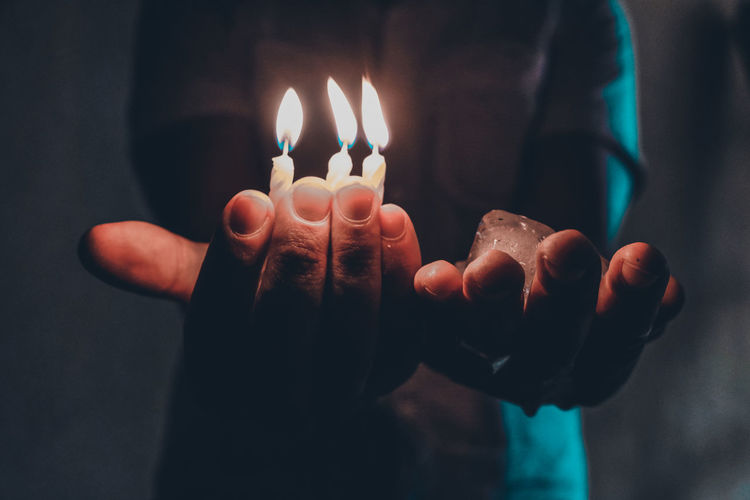 Midsection of man holding burning candles
