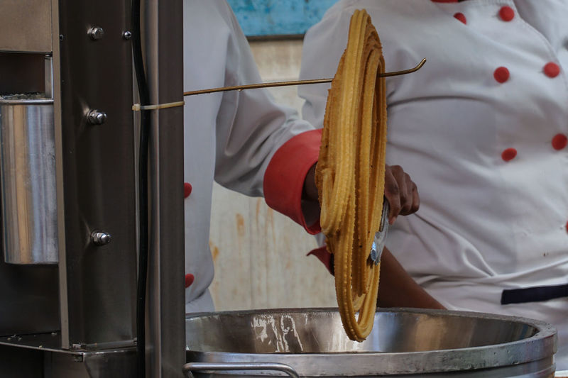 Midsection of chef preparing churro in kitchen