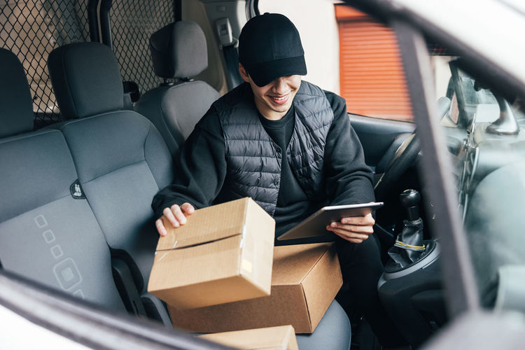 Smiling delivery person with parcel sitting in car