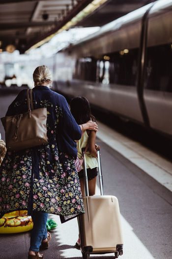 Rear view of mother and daughter walking with luggage on railroad station platform