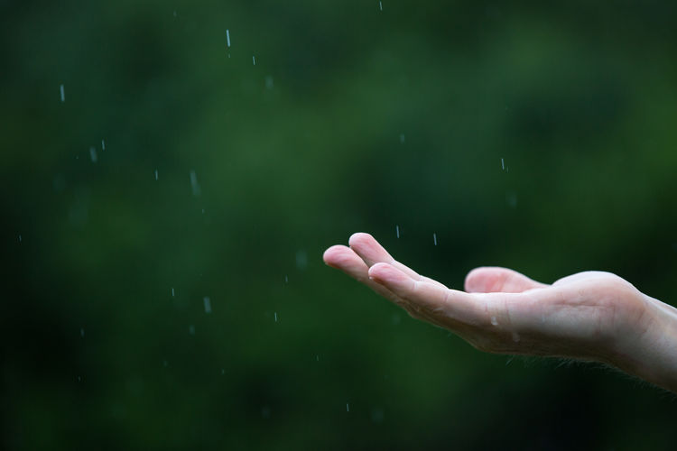 Cropped image of person with raindrops falling on hand