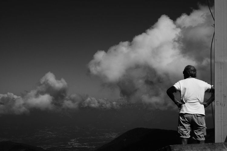 Rear view of man standing by sea against cloudy sky
