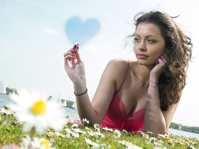 Beautiful woman holding flower with heart shape in sky