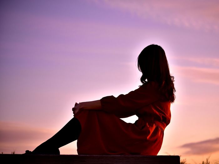 Silhouette woman sitting against orange sky