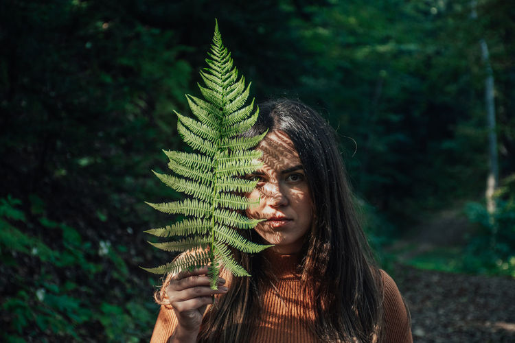 Earth tones portrait of beautiful young woman holding fern leaf in front of face