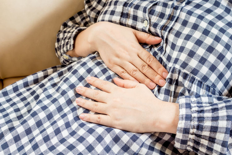 Midsection of woman with stomachache lying on sofa at home
