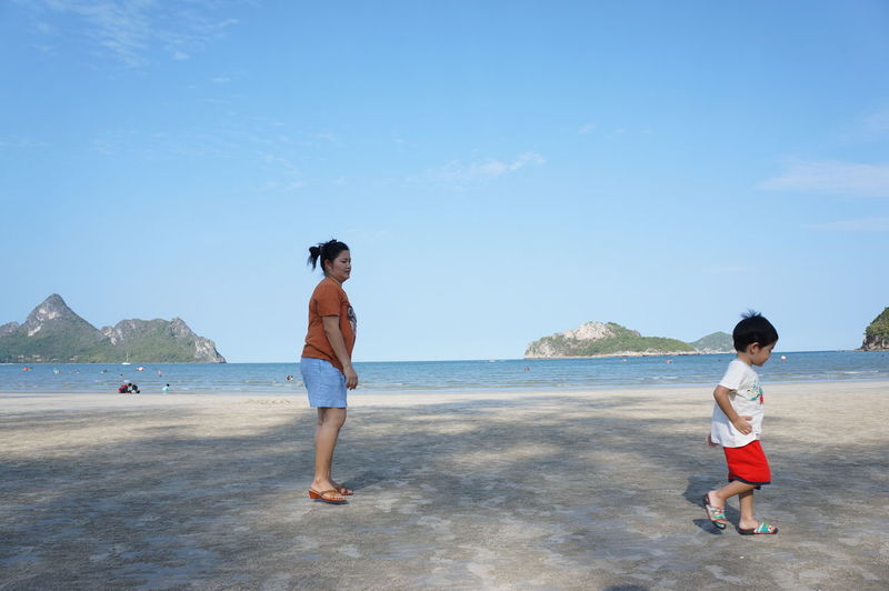 Mother with son enjoying at beach against sky