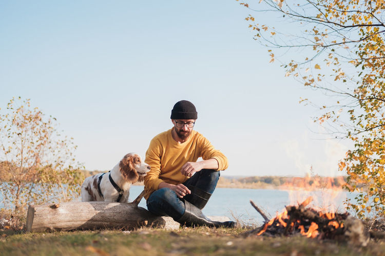 Man with dog sitting against sky