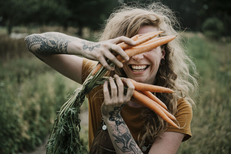 Female farmer smiling while holding carrots at farm