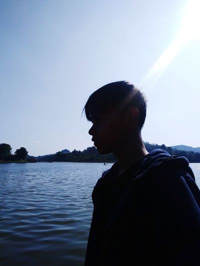 Portrait of young man looking at lake against sky
