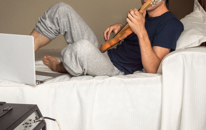 Young man lying on a bed playing electric bass.