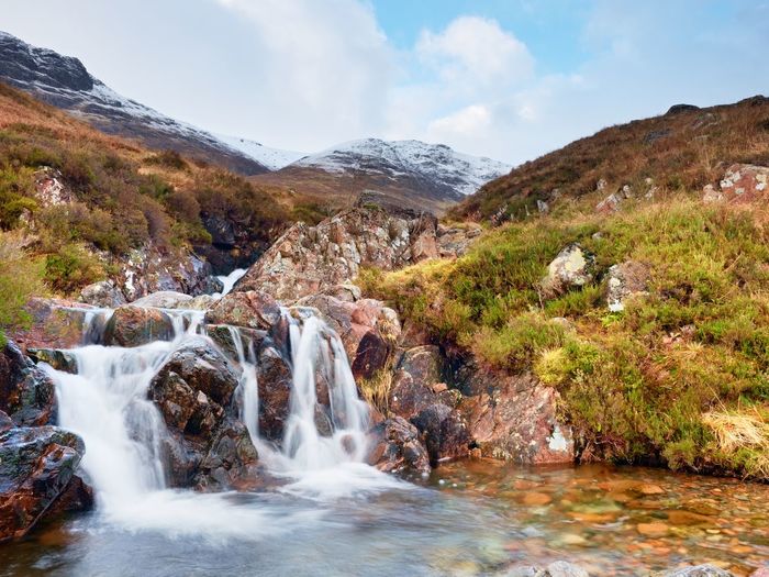 Rapids in waterfall on stream, higland in scotland an early spring. snowy cone of mountain in clouds