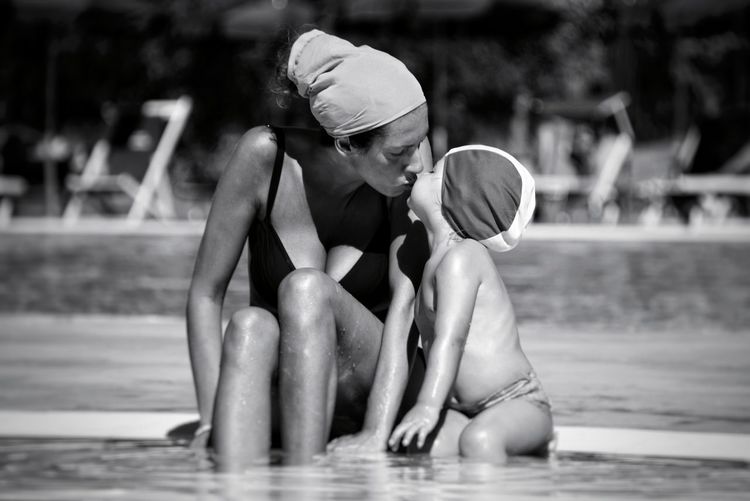 Mother and daughter kissing on mouth while sitting in swimming pool