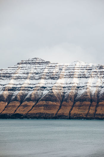 Majestic scenery of rocky terrain covered with snow near calm sea on cloudy day on faroe islands