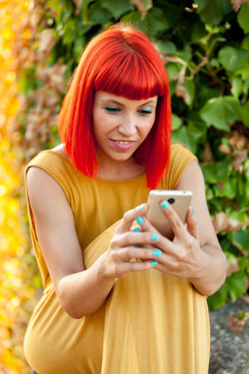 Close-up of smiling woman using smart phone against plants
