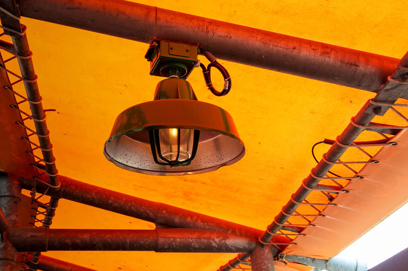 Low angle view of yellow lamp hanging against orange wall