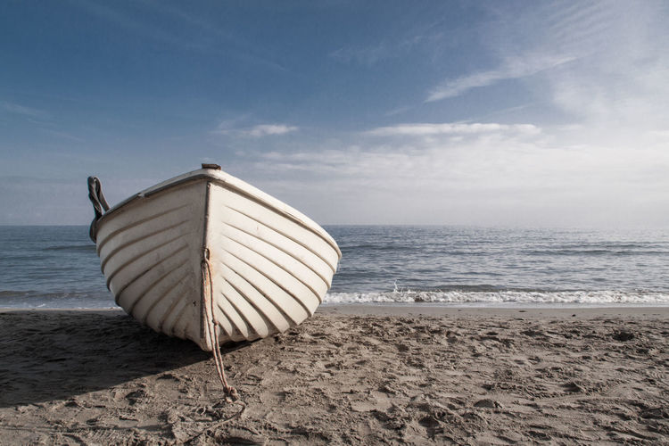 Boat moored at beach against sky on sunny day