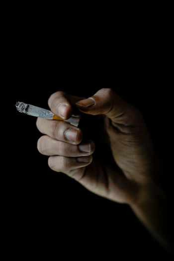 Close-up of hand holding cigarette over black background