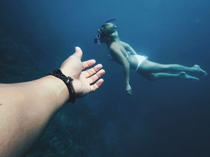 Cropped hand of man gesturing at female friend snorkeling in sea