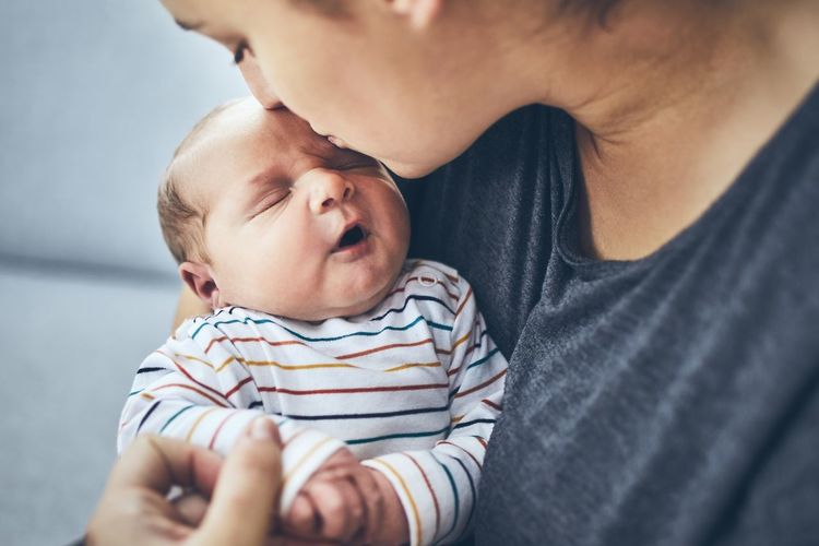 Close-up of woman kissing newborn son while sitting on sofa at home