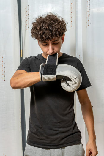 Young man wearing boxing glove standing against wall