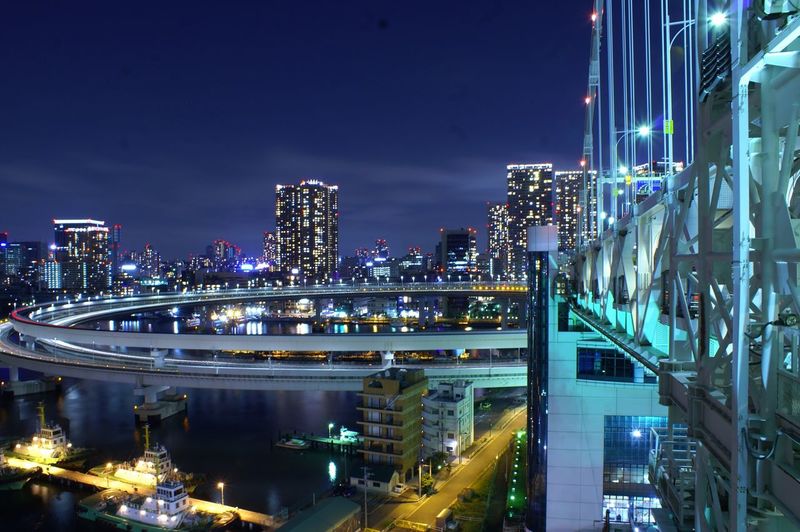 Illuminated bridge and buildings against sky at night