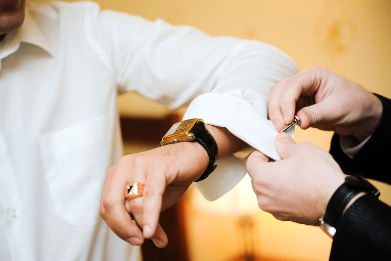 Cropped hand of man putting cuff link on bridegroom