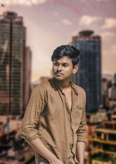 Portrait of young man standing against buildings in city