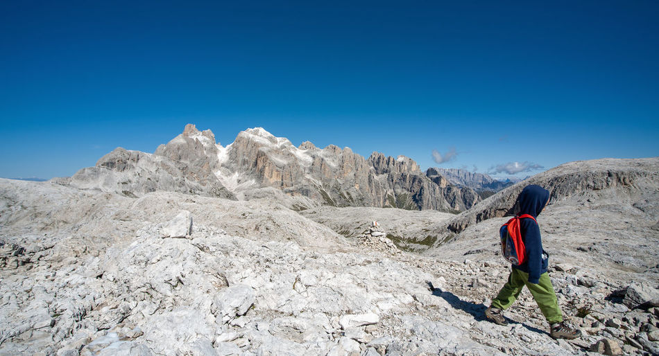 Rear view of man standing on mountain against clear blue sky
