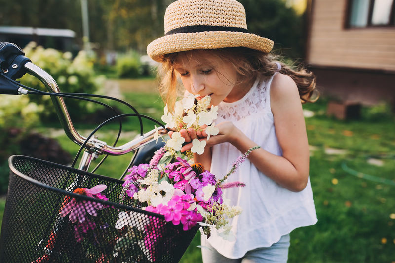 Smiling girl smelling flowers in bicycle against trees