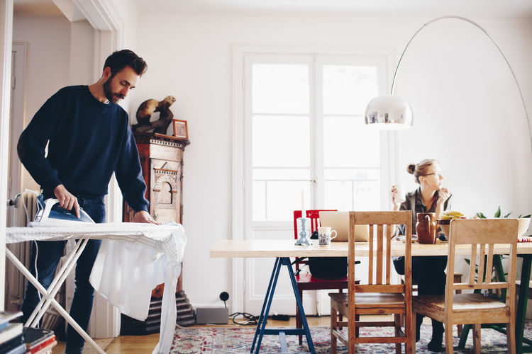 Man ironing while woman looking away in dining room at home
