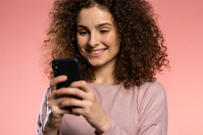 Portrait of smiling woman holding smart phone against pink background