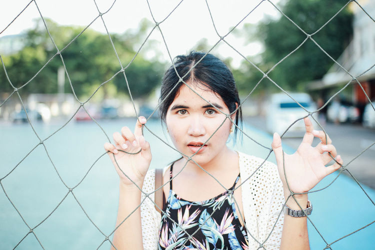 Portrait of young woman standing behind chainlink fence