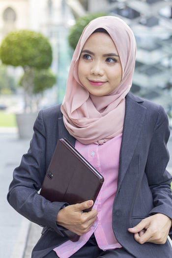Thoughtful businesswoman holding digital tablet in city