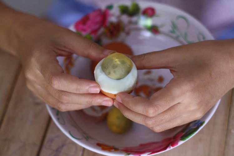 Midsection of woman holding boiled egg over plate at table