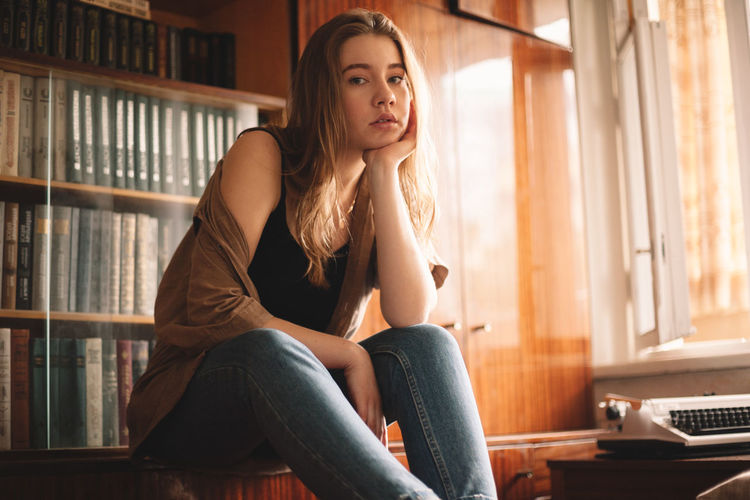 Young woman sitting by bookshelf