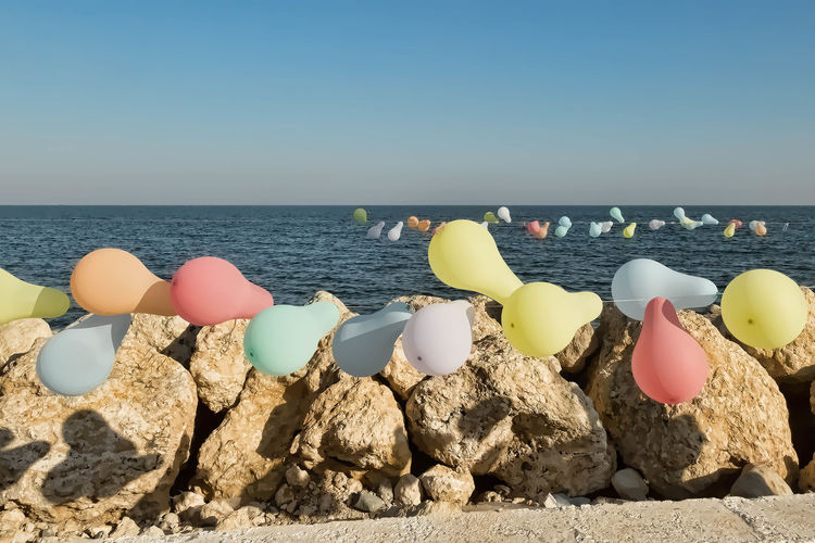 Colorful balloons tied with rope on rock against sea during sunny day