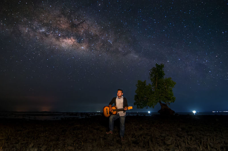 Man playing guitar while standing on land against sky at night