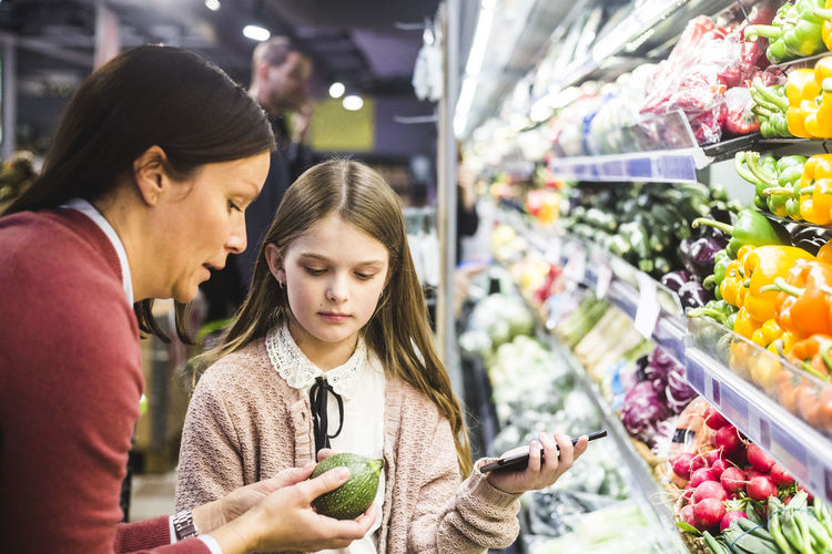 Mother showing cucumber to daughter while grocery shopping in supermarket
